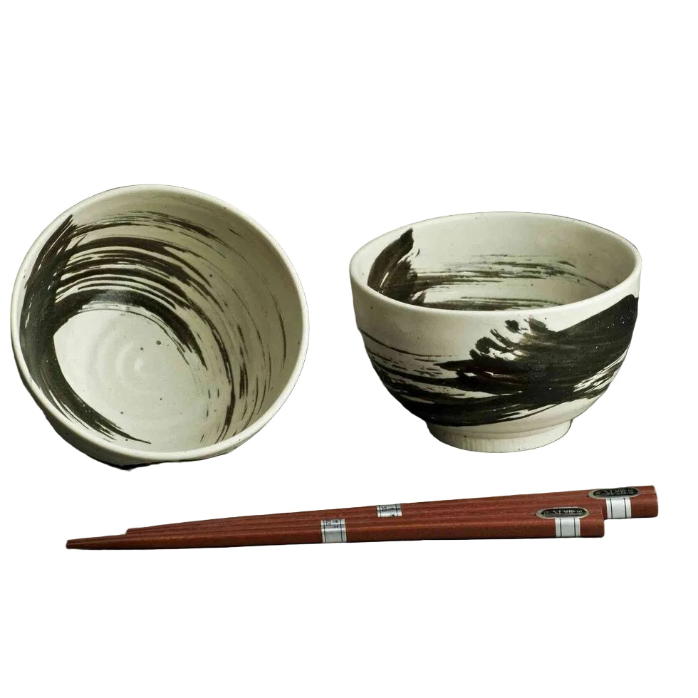 A ceramic bowl set with a matching chopstick holder, featuring a white glaze with black brushstroke patterns, accompanied by reddish-brown wooden chopsticks with silver bands.